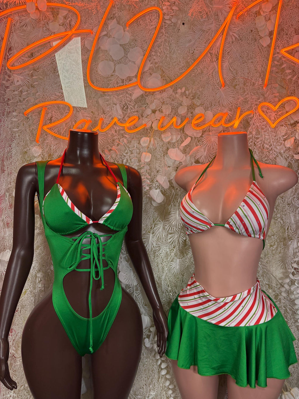 Green lace-up bodysuit and red/white striped top with green skirt, both shown on mannequins