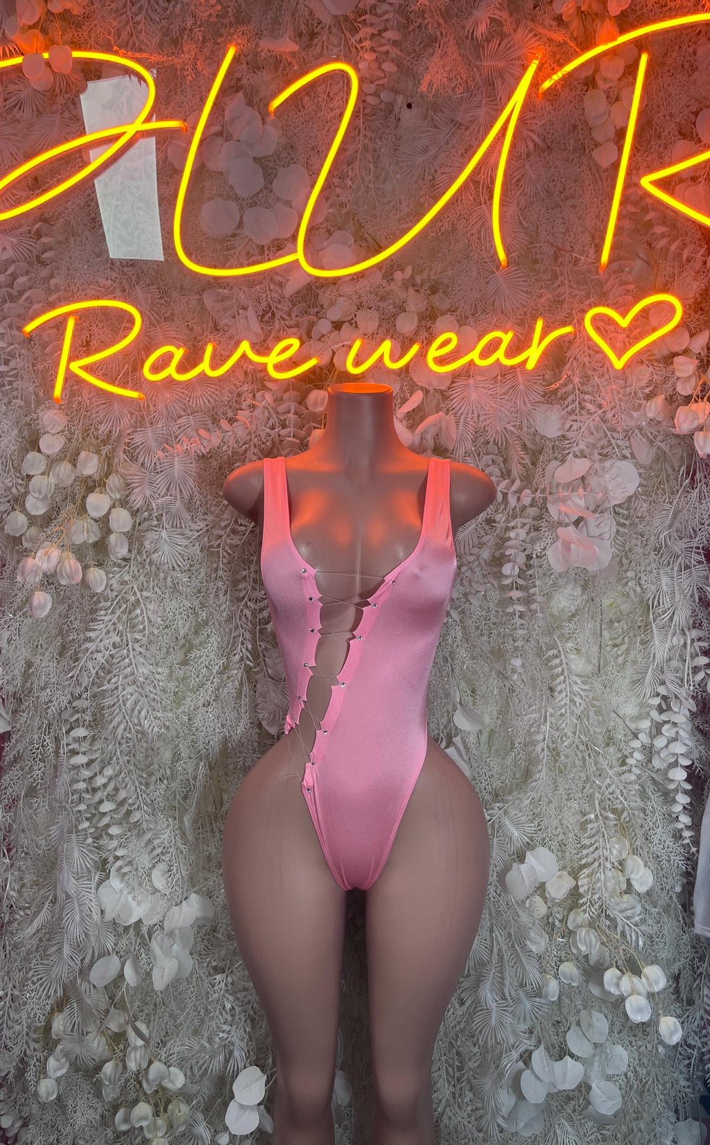 Pink sleeveless thong bodysuit with lace front detail, shown on a mannequin