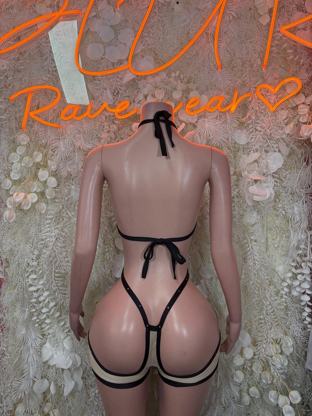 Tan strappy bodysuit with open back, black trim, and bow at center