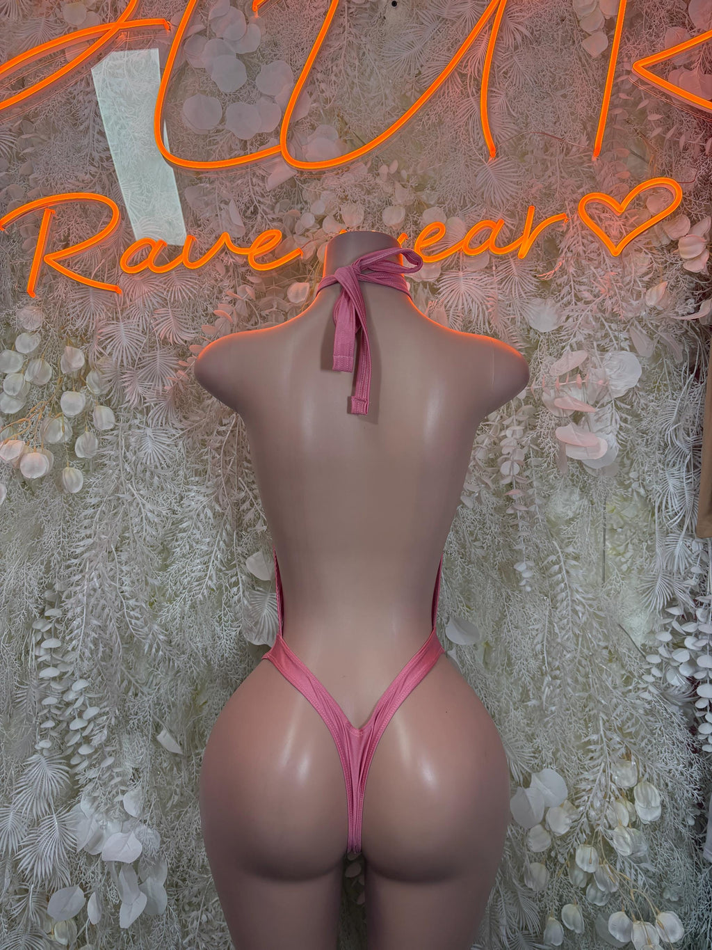 Pink halter bodysuit with open back, bow neck tie, and chain tassel detail