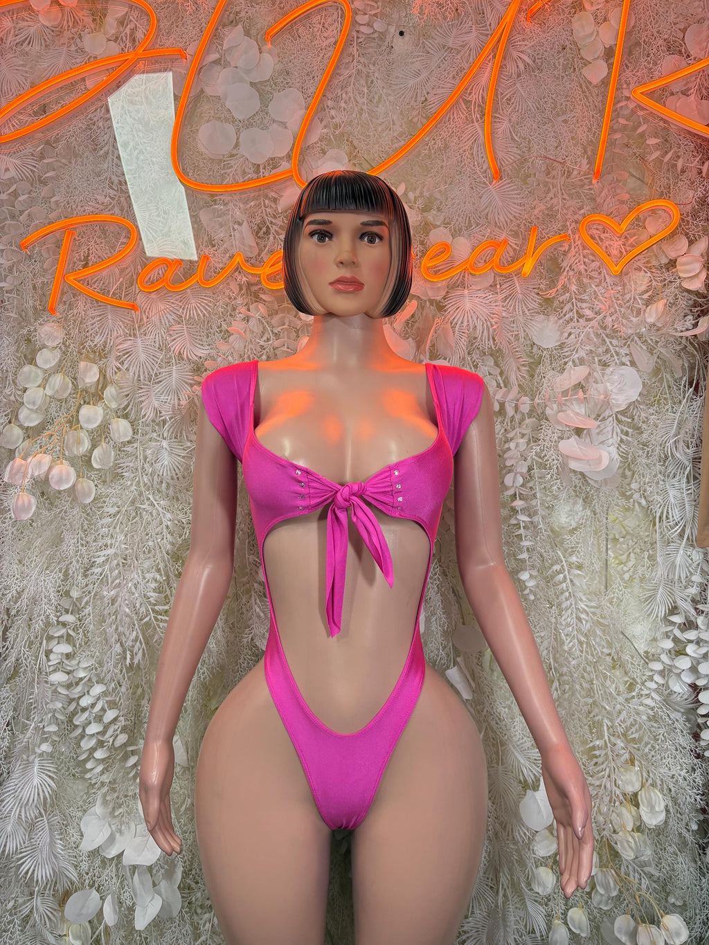 Pink one-piece bodysuit with V neckline, ruched center bow, and high-cut legs