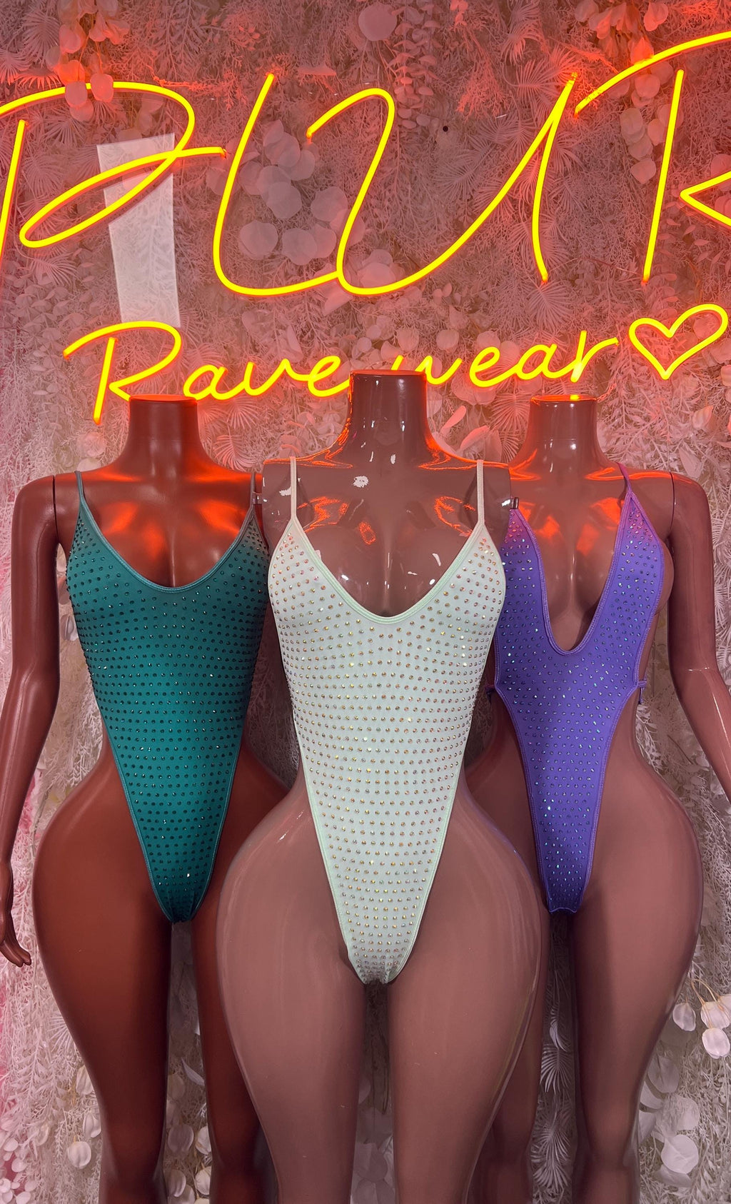 Three rhinestone one-piece bodysuits: teal, white, and deep purple V-neck style
