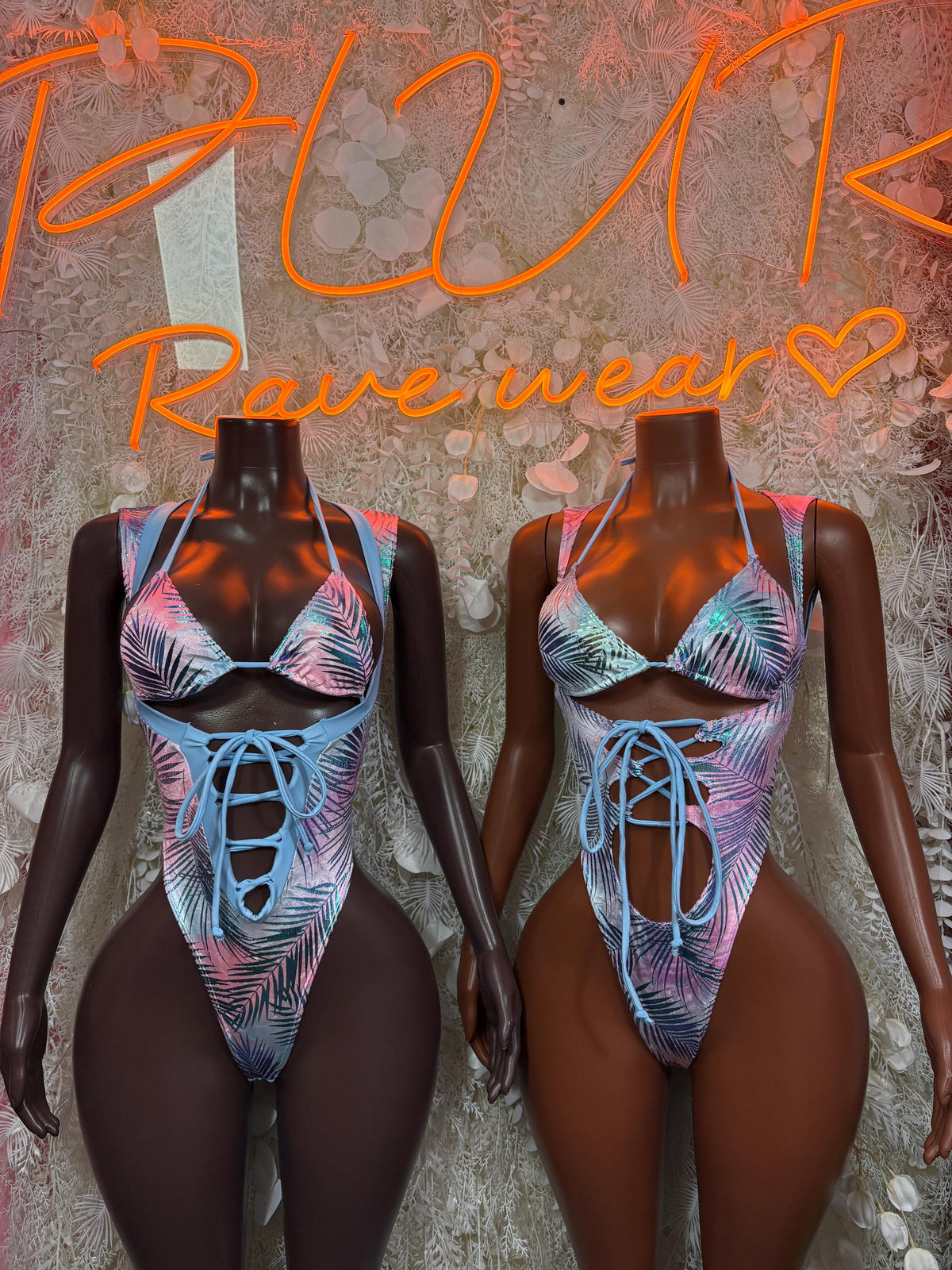 Two women wearing blue tropical print bodysuits with lace-up front and high-cut legs
