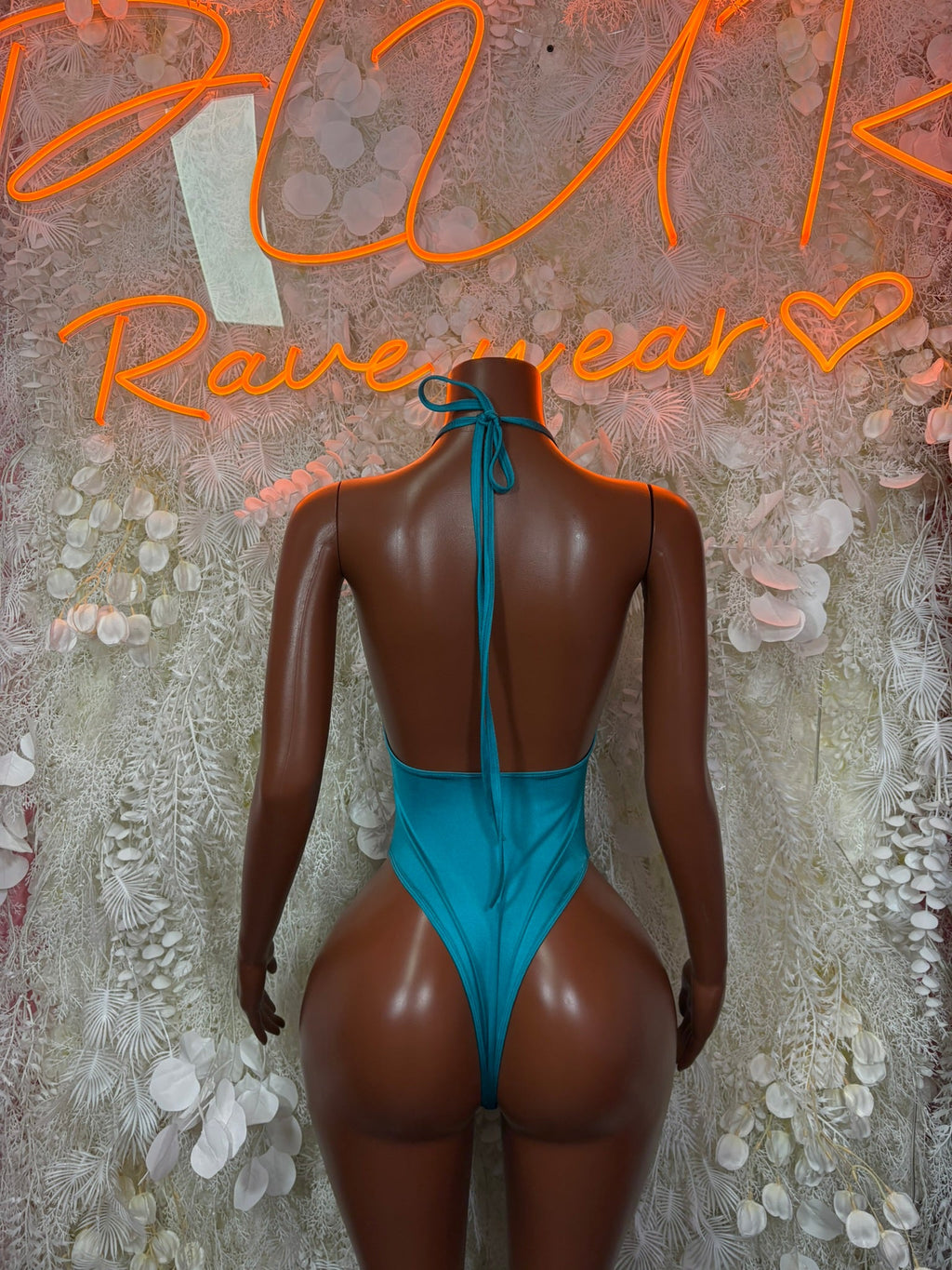 Teal one-shoulder bodysuit with open back, crisscross straps, and tie-back detail